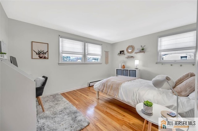 bedroom with multiple windows, wood finished floors, and baseboard heating