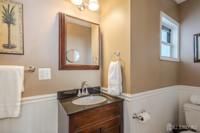 bathroom featuring vanity, toilet, and a wainscoted wall