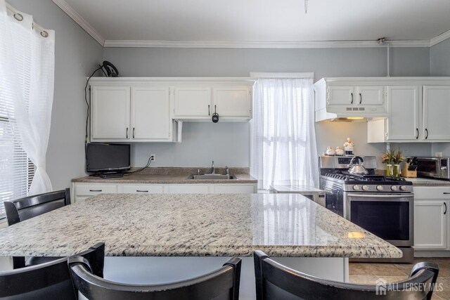 kitchen with under cabinet range hood, stainless steel range with gas stovetop, and white cabinets