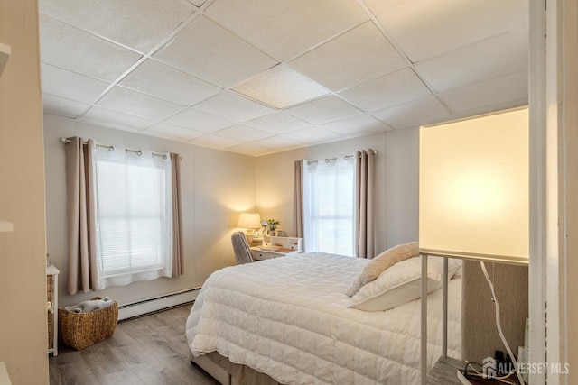 bedroom featuring a drop ceiling, wood finished floors, and baseboard heating