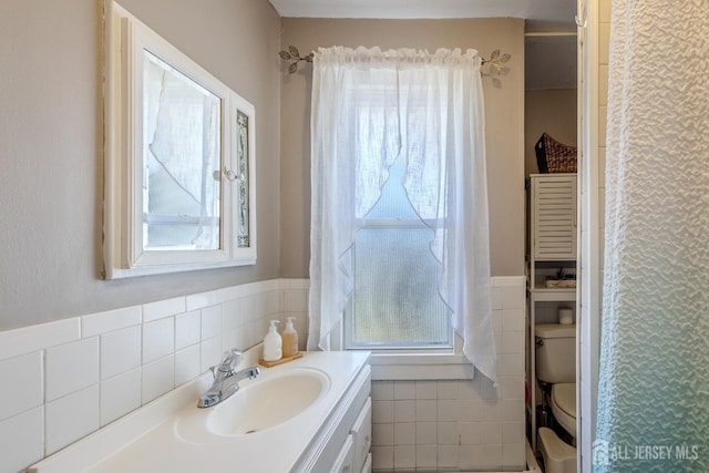 full bath with vanity, tile walls, toilet, and a wainscoted wall