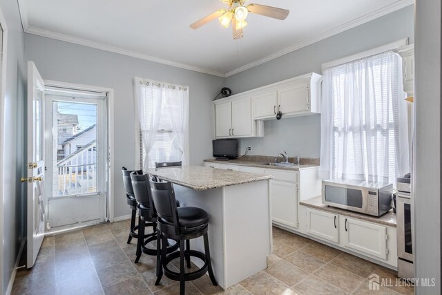 kitchen with a wealth of natural light, stainless steel microwave, white cabinetry, and a sink
