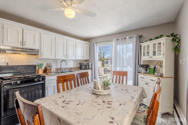 kitchen featuring gas stove, white cabinetry, under cabinet range hood, and a sink