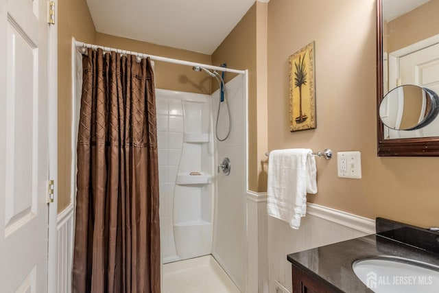 bathroom featuring a shower with shower curtain, vanity, and wainscoting