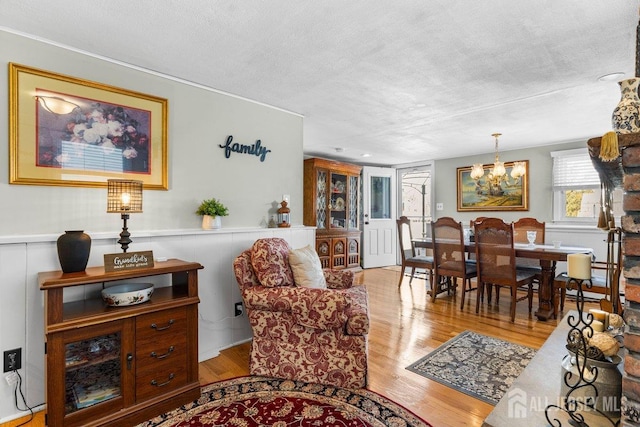 living area with light wood finished floors, a notable chandelier, a textured ceiling, and wainscoting