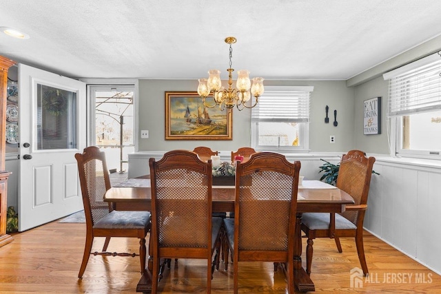 dining area with light wood-type flooring, wainscoting, a textured ceiling, and an inviting chandelier