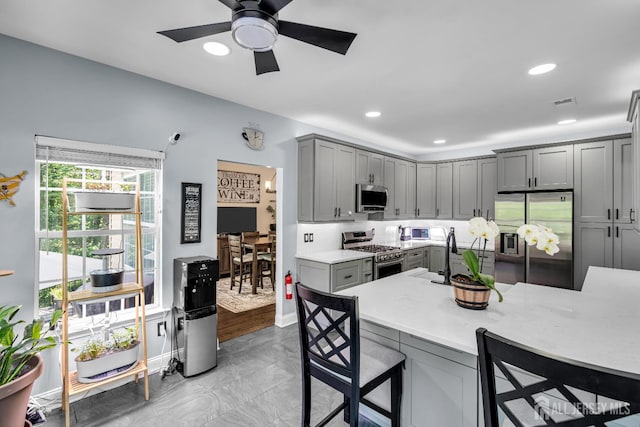 kitchen with stainless steel appliances, gray cabinets, a kitchen breakfast bar, light countertops, and ceiling fan