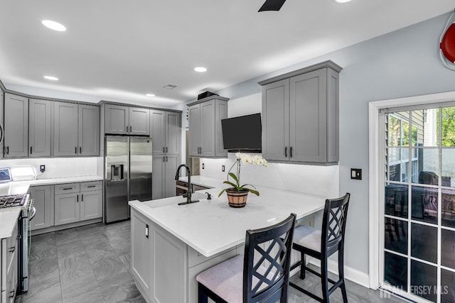 kitchen with stainless steel appliances, a sink, gray cabinetry, backsplash, and light marble finish floors