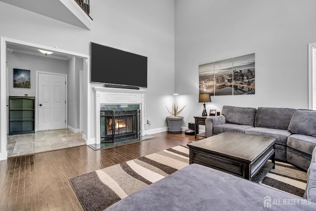 living area featuring a towering ceiling, wood finished floors, a premium fireplace, and baseboards
