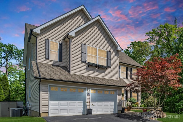 traditional-style house with an attached garage, driveway, central AC unit, and roof with shingles