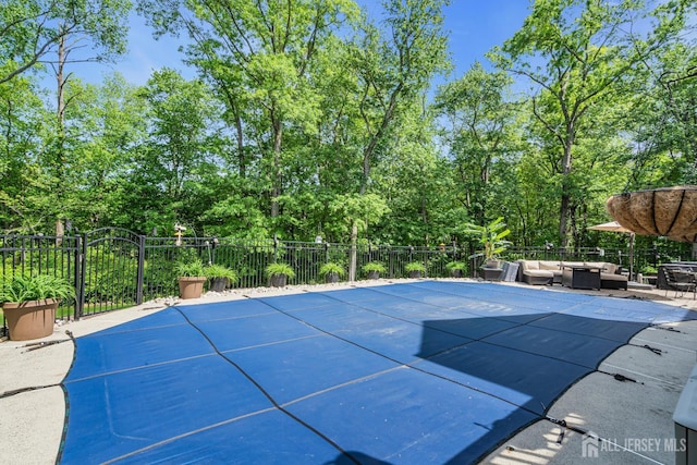 view of pool with an outdoor hangout area, fence, and view of scattered trees