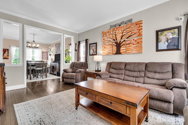 living area featuring wood-type flooring, a chandelier, crown molding, and baseboards