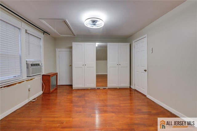 unfurnished bedroom with cooling unit, multiple closets, and hardwood / wood-style floors