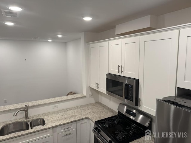 kitchen featuring visible vents, light stone countertops, white cabinets, stainless steel appliances, and a sink