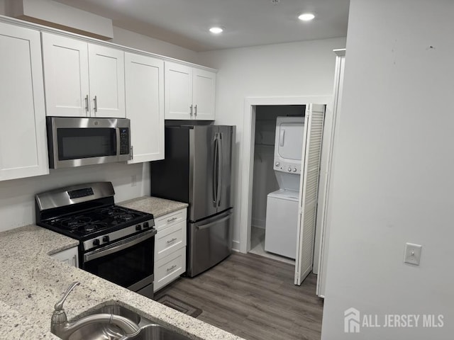 kitchen with light stone counters, stainless steel appliances, stacked washing maching and dryer, white cabinetry, and dark wood-style flooring