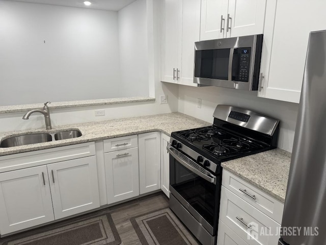 kitchen with light stone counters, dark wood-style floors, a sink, stainless steel appliances, and white cabinetry