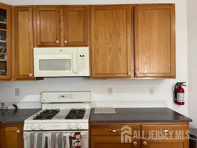 11 Pebble Beach Ct, Monroe, NJ 08831 - kitchen with white appliances, brown cabinets, dark countertops, and glass insert cabinets