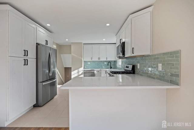 kitchen featuring tasteful backsplash, appliances with stainless steel finishes, a peninsula, white cabinets, and light countertops