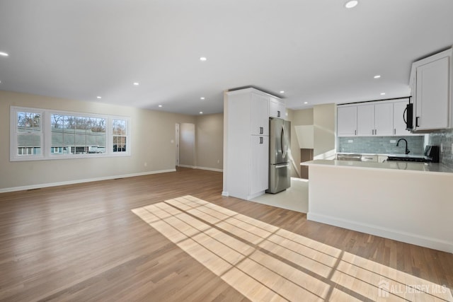 kitchen featuring backsplash, open floor plan, freestanding refrigerator, black microwave, and light wood finished floors