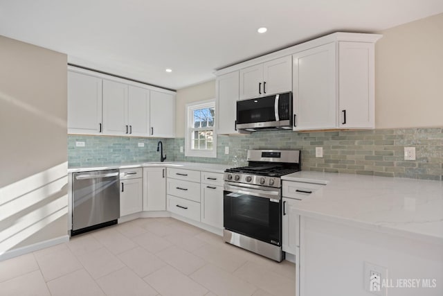 kitchen featuring light stone counters, decorative backsplash, appliances with stainless steel finishes, white cabinetry, and a sink