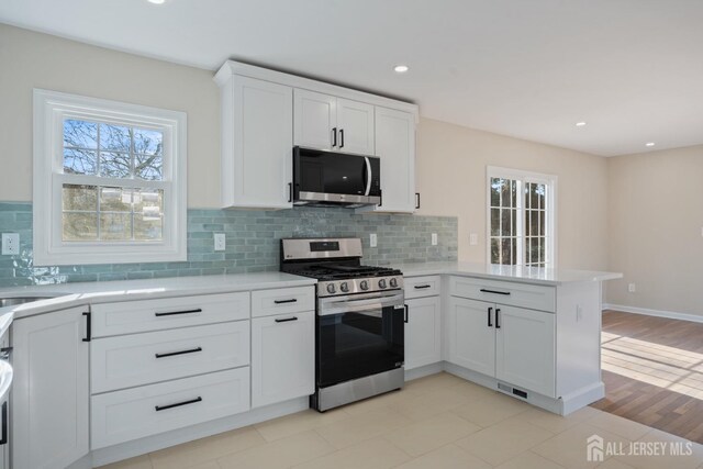 kitchen featuring stainless steel appliances, a peninsula, light countertops, and white cabinetry