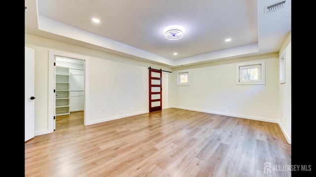 interior space with a barn door, a raised ceiling, and light wood-type flooring