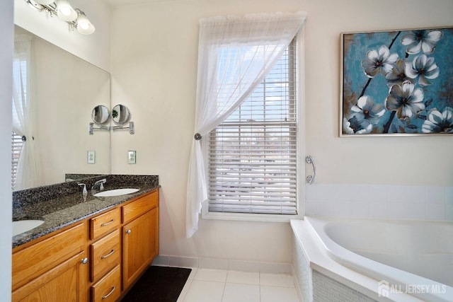 bathroom featuring baseboards, a garden tub, double vanity, tile patterned floors, and a sink