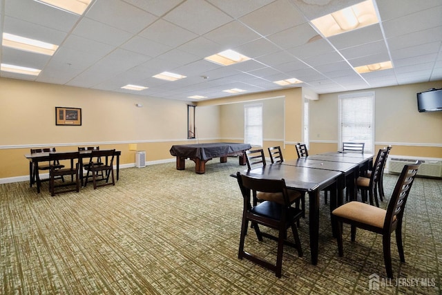 carpeted dining space featuring a drop ceiling, baseboards, and an AC wall unit