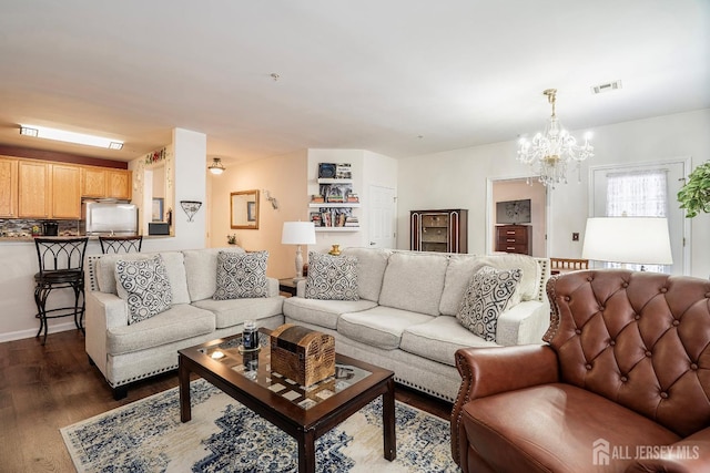 living area with dark wood finished floors, visible vents, and an inviting chandelier