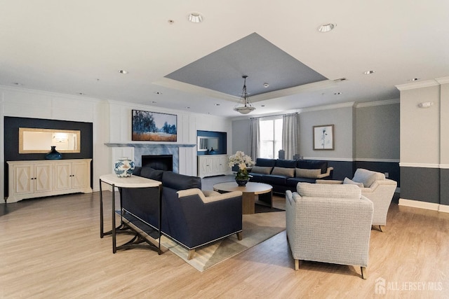 living area with visible vents, crown molding, light wood-type flooring, a tray ceiling, and a premium fireplace