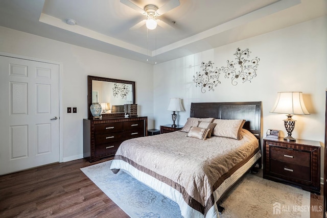 bedroom with a tray ceiling, wood finished floors, baseboards, and ceiling fan