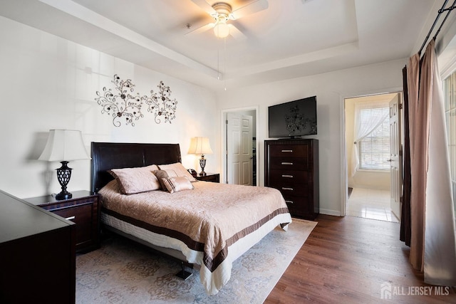 bedroom featuring a ceiling fan, a raised ceiling, wood finished floors, and baseboards