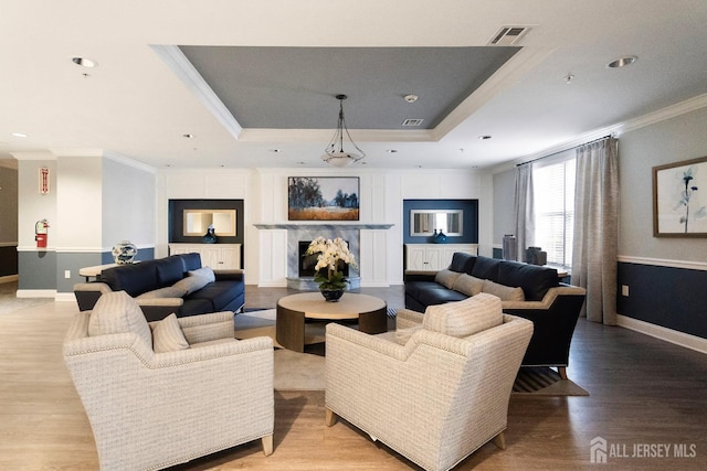 living area featuring a tray ceiling, visible vents, light wood-style floors, and ornamental molding