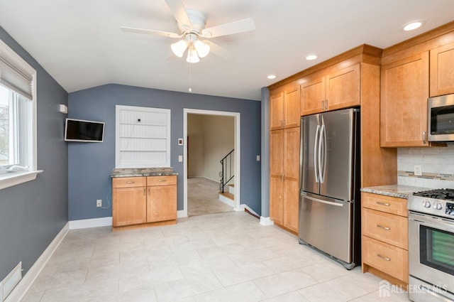 kitchen with lofted ceiling, backsplash, ceiling fan, light stone countertops, and appliances with stainless steel finishes