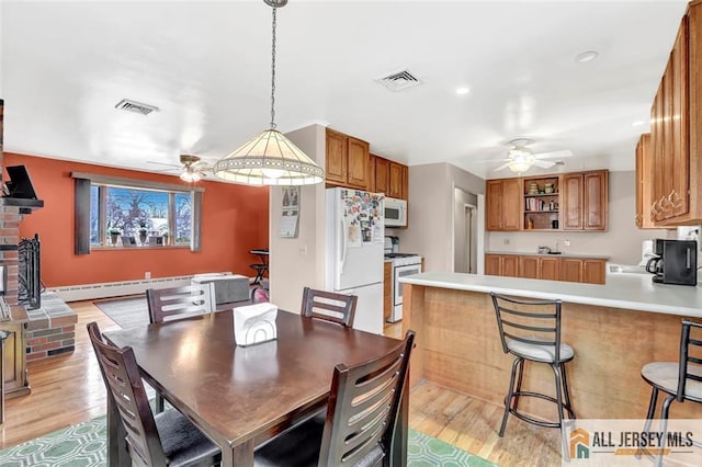 dining area with a baseboard radiator, visible vents, ceiling fan, and light wood finished floors