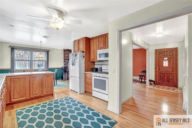 kitchen with white appliances, light countertops, light wood-style floors, and decorative light fixtures