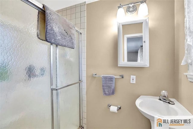 bathroom with a shower with shower door and a sink