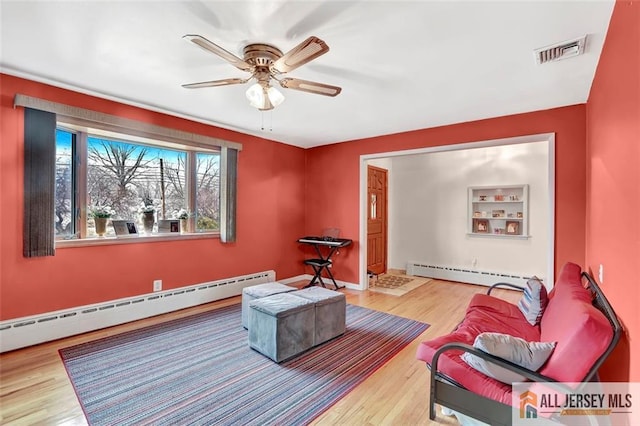 living area with light wood-style floors, ceiling fan, visible vents, and baseboard heating