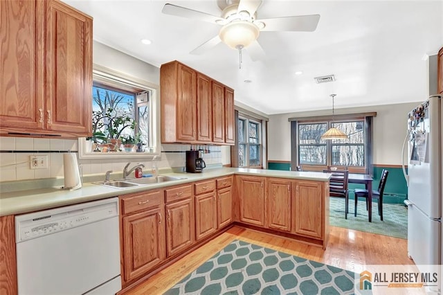 kitchen featuring a peninsula, white appliances, light countertops, a wealth of natural light, and decorative light fixtures