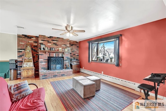 living room featuring a baseboard heating unit, a fireplace, wood finished floors, visible vents, and a ceiling fan