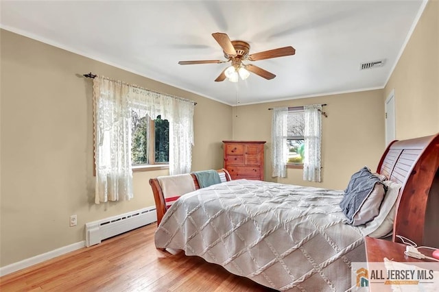 bedroom with a baseboard radiator, visible vents, baseboards, light wood finished floors, and crown molding