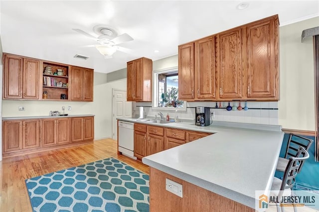 kitchen with brown cabinetry, light countertops, white dishwasher, and open shelves