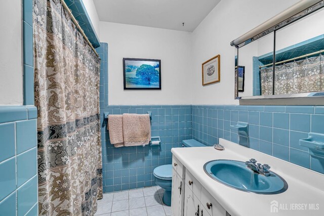 bathroom with vanity, a shower with curtain, tile patterned flooring, toilet, and tile walls