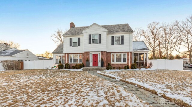 colonial inspired home featuring a chimney, a sunroom, brick siding, and fence