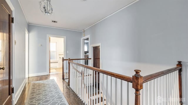 hall featuring wood finished floors, visible vents, baseboards, ornamental molding, and an upstairs landing