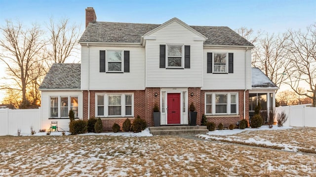 colonial inspired home with fence, brick siding, and a chimney