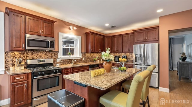 kitchen featuring light stone counters, visible vents, appliances with stainless steel finishes, and a kitchen breakfast bar