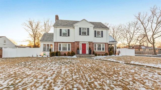 colonial home featuring brick siding, a chimney, and fence