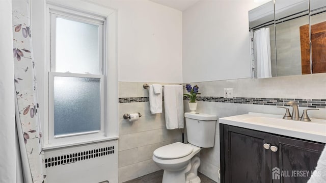 bathroom with toilet, tile walls, wainscoting, vanity, and radiator heating unit