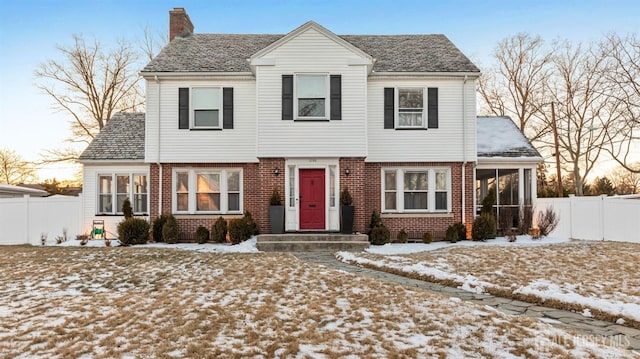 colonial home with a sunroom, brick siding, fence, and a chimney